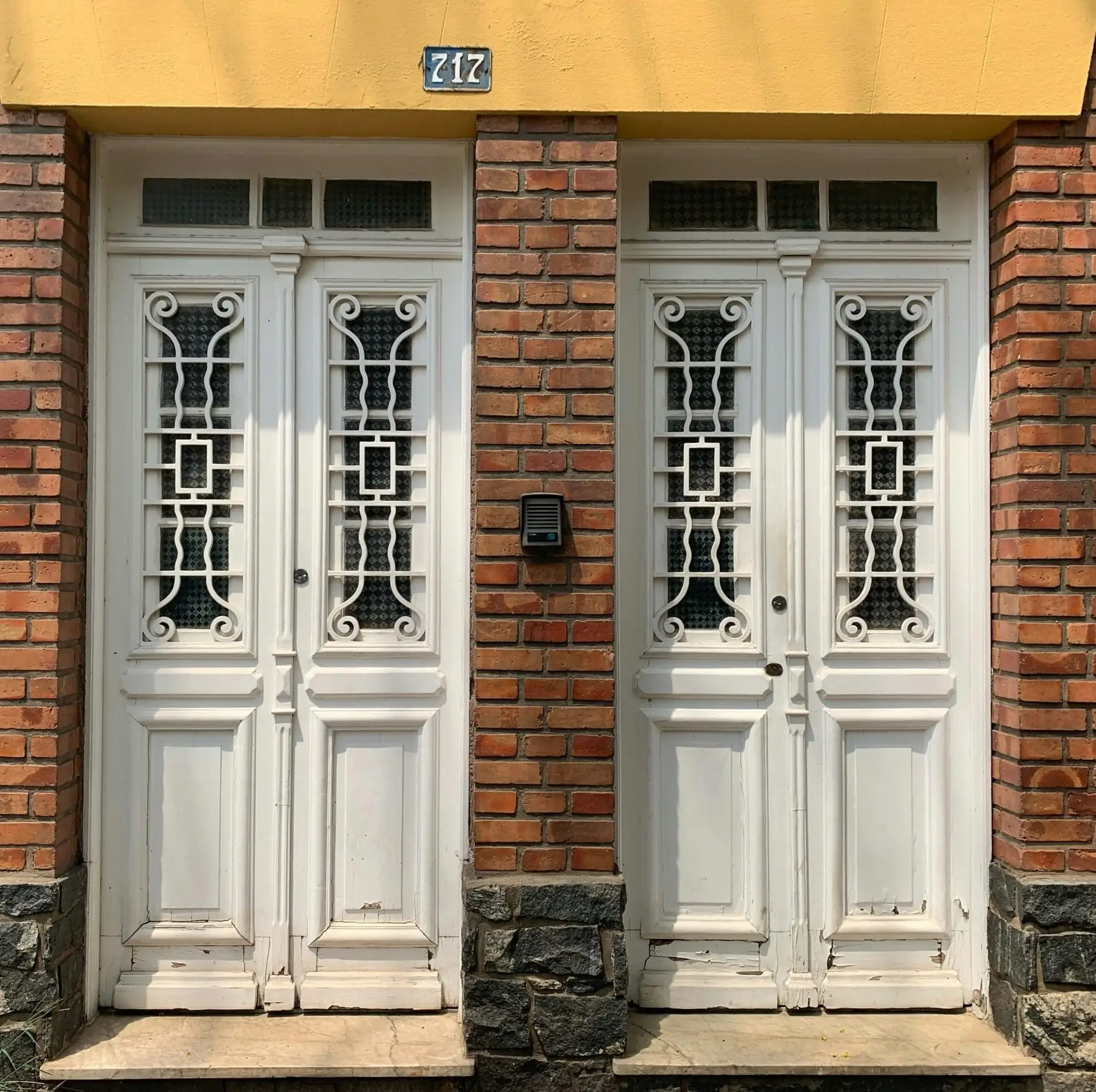 A pair of white wooden double doors with intricate ironwork, with brick restoration, highlighting a blend of classic architecture and craftsmanship.